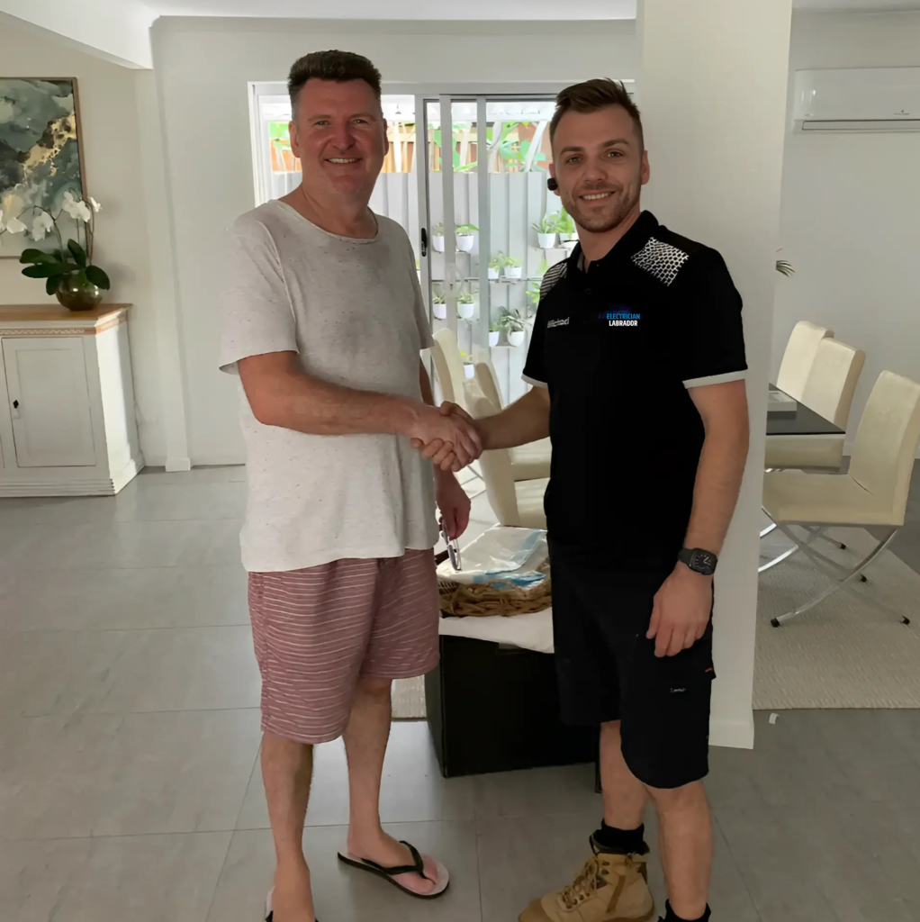 Electrician shaking hands with a client in a home interior, both smiling.
